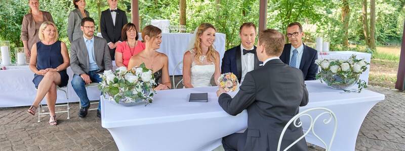 Hochzeitspaar mit Gästen auf der festlich dekorierten Erleninsel sitzend. 