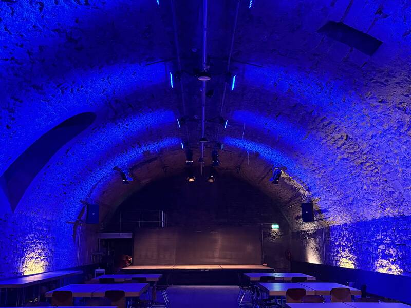 Gewölbekeller Schlosskeller mit Bockbetischung und dunkelblauer Beleuchtung, Blick auf die Bühne. 