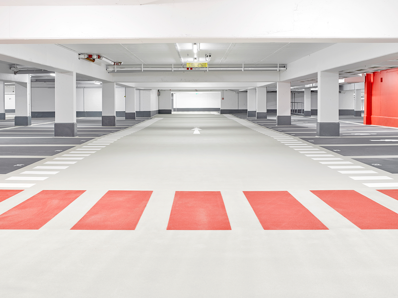 Ein leerer, gut beleuchteter Parkhausbereich mit roten Streifen am Boden, weißen Markierungen und roten Abschnitten an den Wänden.